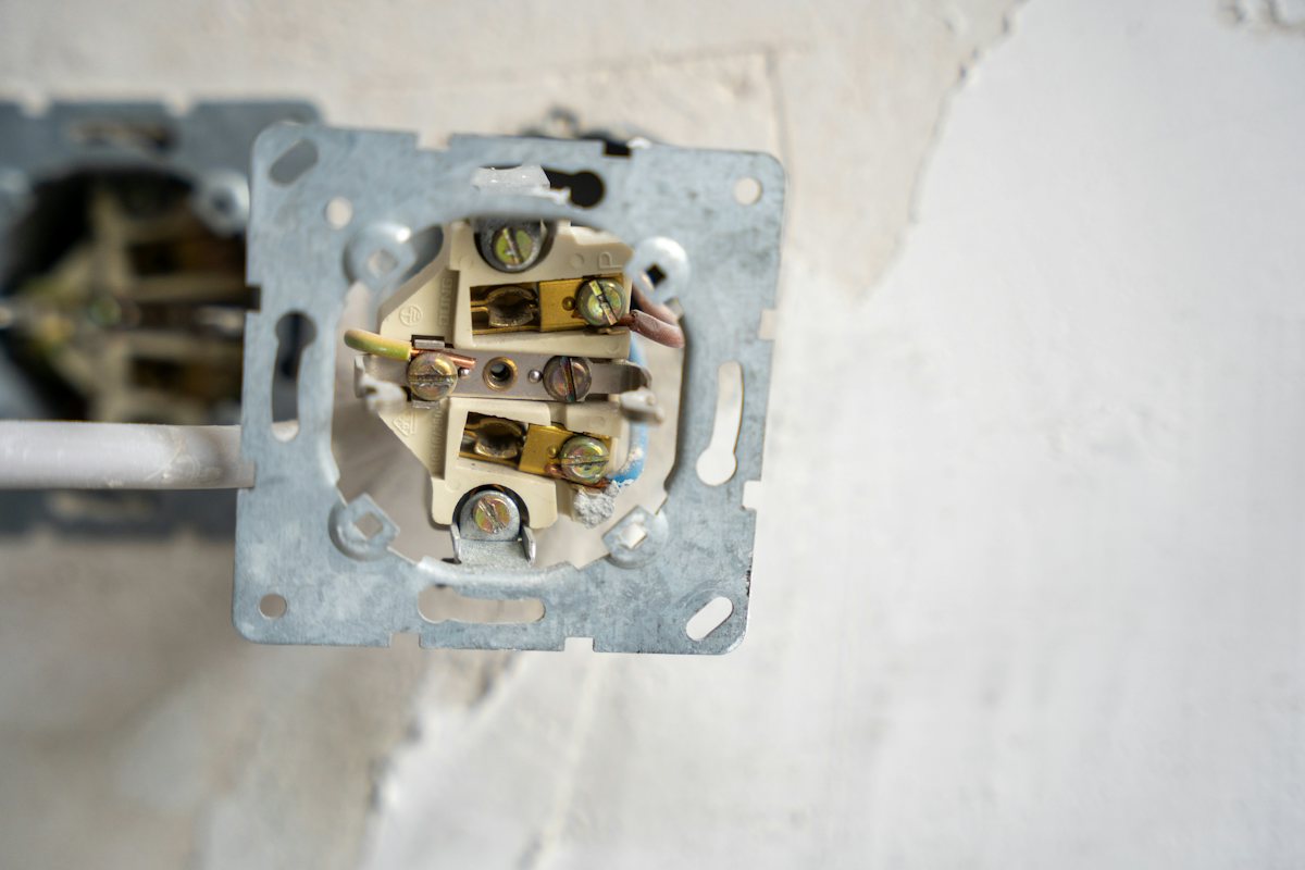 Wall outlet pulled out of the wall with its wires and terminal screws showing