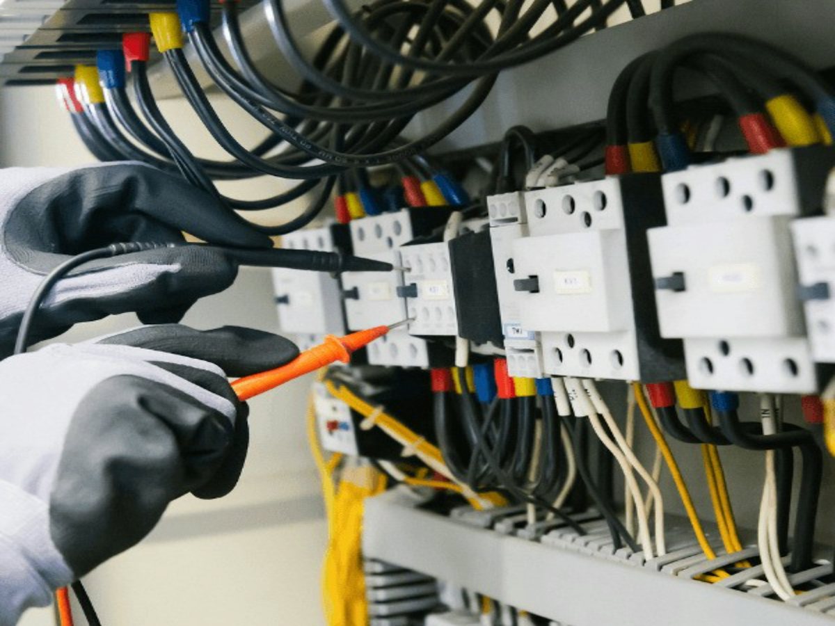 Electrician testing wiring inside a panel with a multimeter